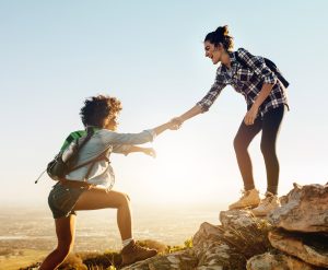 woman extending hand to another woman to climb mountain